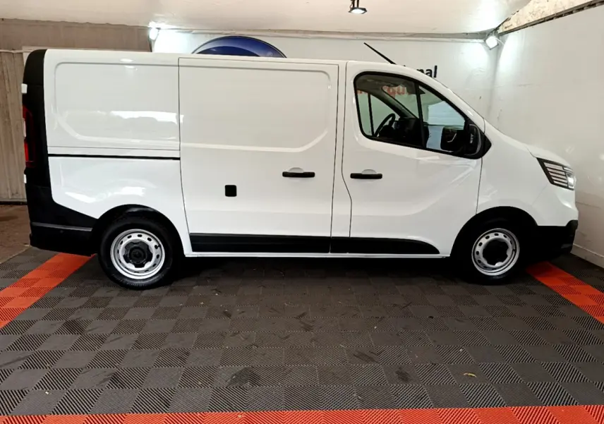 Profil côté gauche d'un fourgon Renault Trafic blanc, avec jantes acier et détails noirs contrastants.
