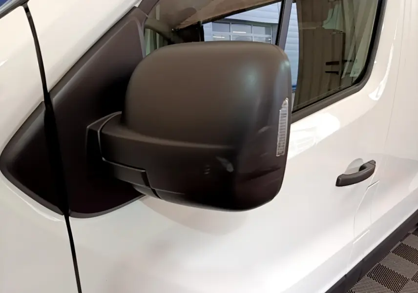 Gros plan sur le rétroviseur noir côté conducteur du Renault Trafic Fourgon blanc, vue latérale avant droite.