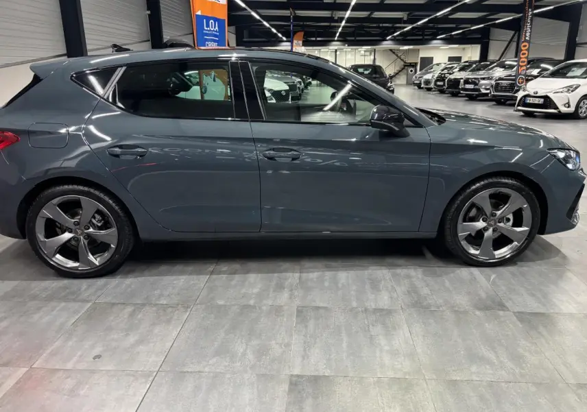 Vue latérale droite d'une CUPRA Leon 2026 bleu Fjord avec jantes alliage 18 pouces en intérieur showroom.