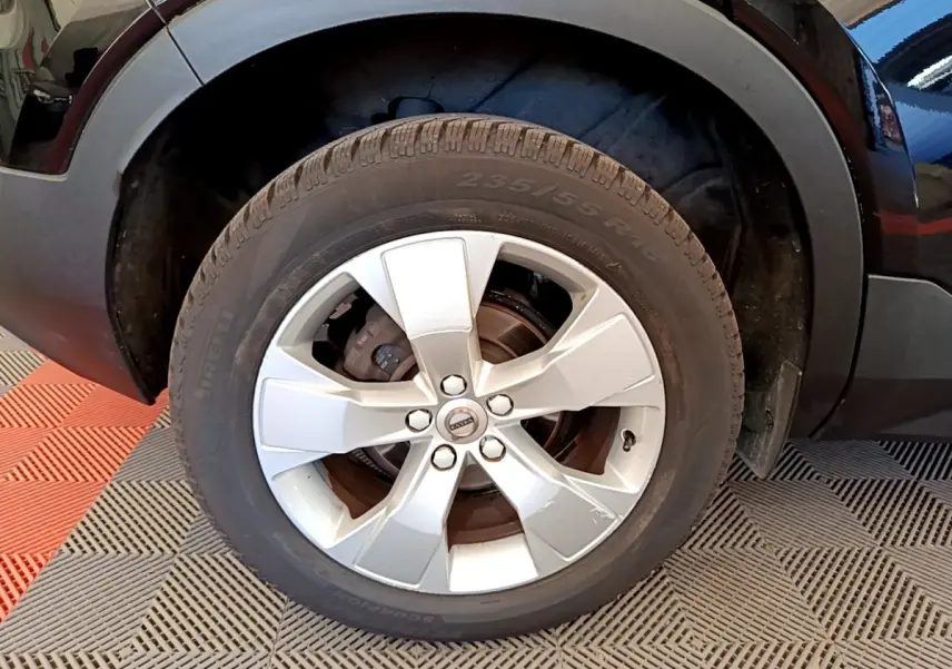 Gros plan sur la roue avant droite d’un Volvo XC40 noir, jante alliage argentée avec logo Volvo au centre.