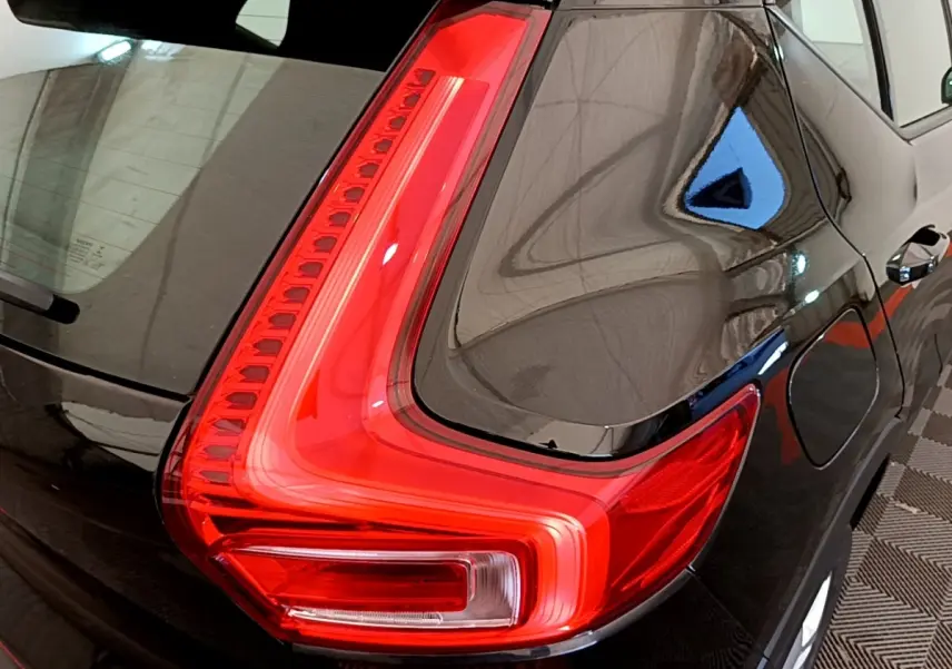 Gros plan sur le feu arrière gauche rouge vif d’un Volvo XC40 noir, mettant en valeur la carrosserie brillante.