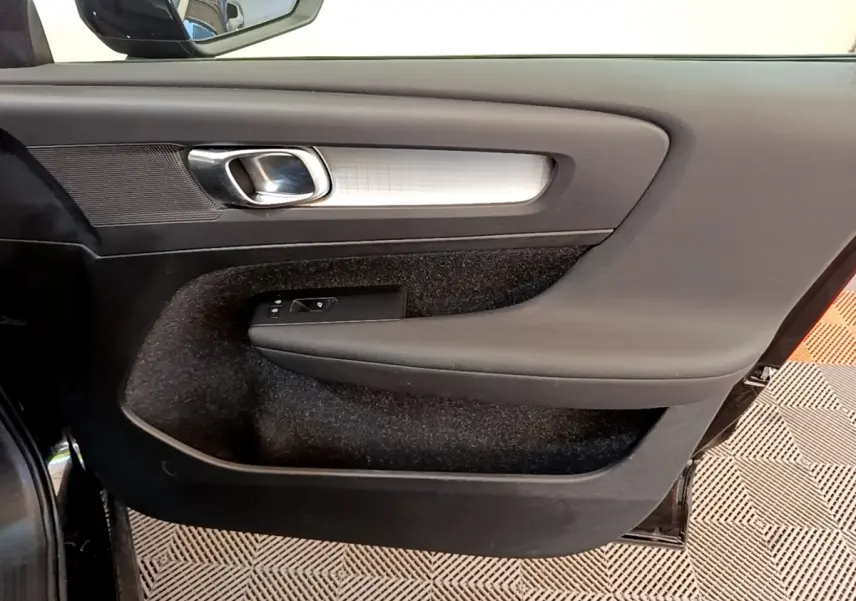 Vue rapprochée de la porte intérieure côté gauche du Volvo XC40 noir, avec poignée argentée et commandes de fenêtre.