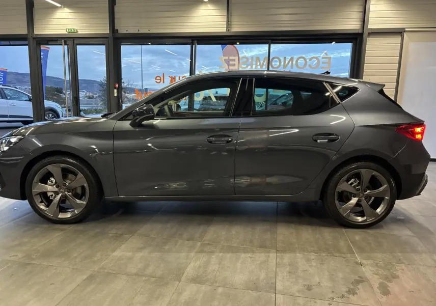 Vue de profil droit d'une CUPRA Leon 2.0 TDI gris magnetic avec jantes alliage 18 pouces en intérieur showroom.