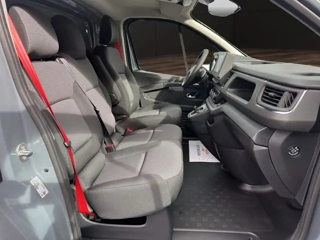 Vue intérieure côté conducteur du Renault Trafic Fourgon gris urbain, montrant les sièges avant et le tableau de bord moderne.