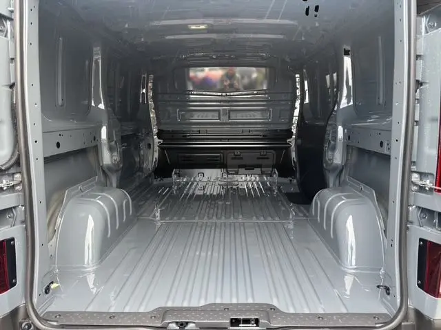 Vue intérieure arrière du Renault Trafic Fourgon gris urbain, montrant l'espace de chargement vide avec cloison et tablette fixe.