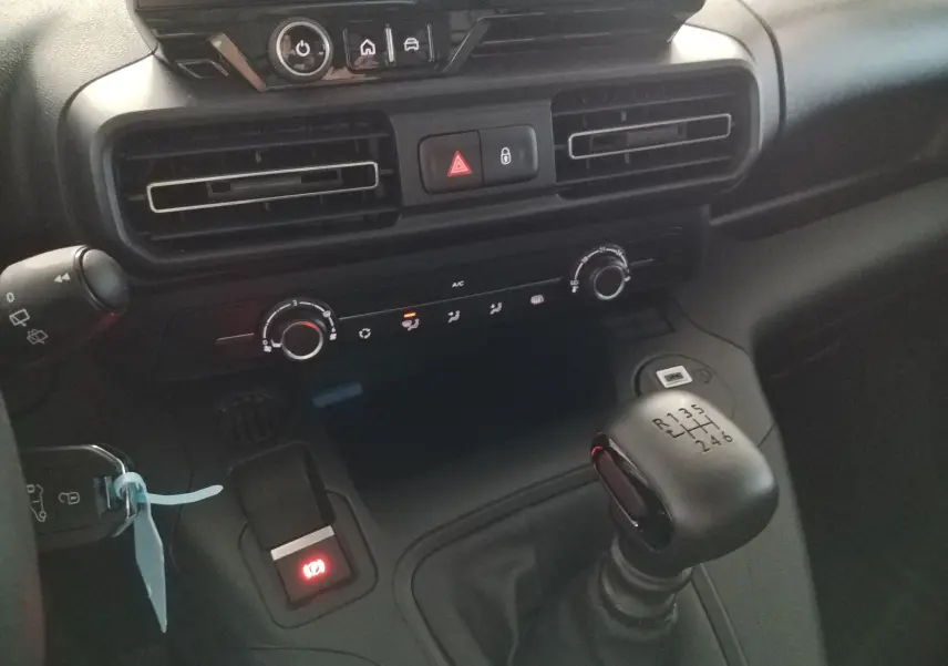 Vue rapprochée de la console centrale intérieure noire du Peugeot Partner blanc, avec levier de vitesses manuel et commandes de climatisation.