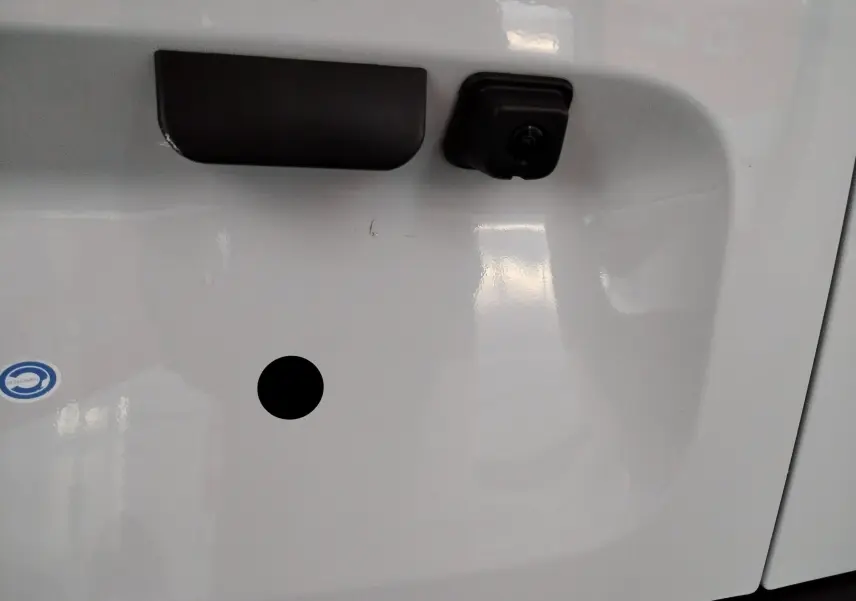 Gros plan sur la poignée et la caméra de recul noire sur la porte arrière blanche du Peugeot Partner FGN 2025.