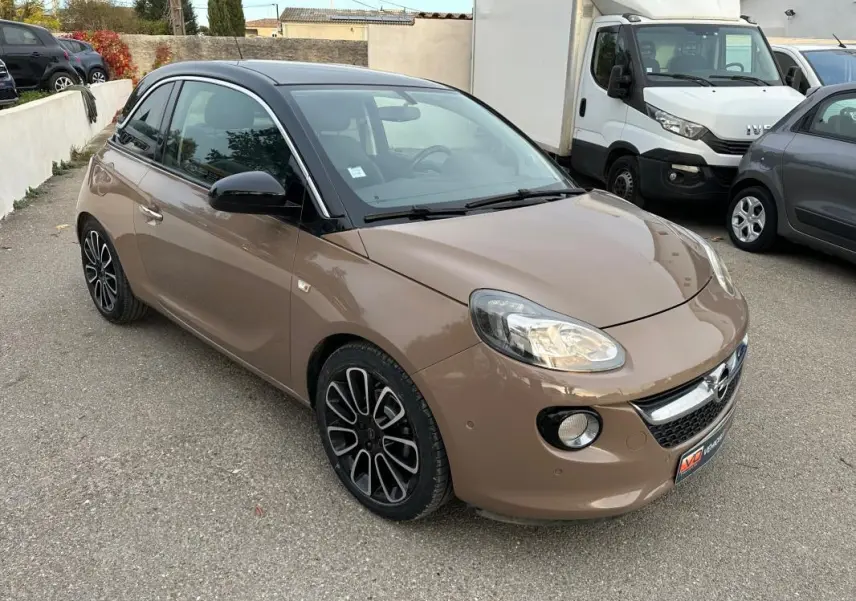 Opel Adam marron vue 3/4 avant droit, toit noir, jantes alliage 16 pouces et phares allumés sur parking.