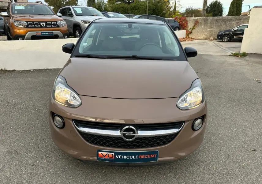 Vue avant d'une Opel Adam marron 2016 avec phares allumés et calandre chromée sur parking extérieur.