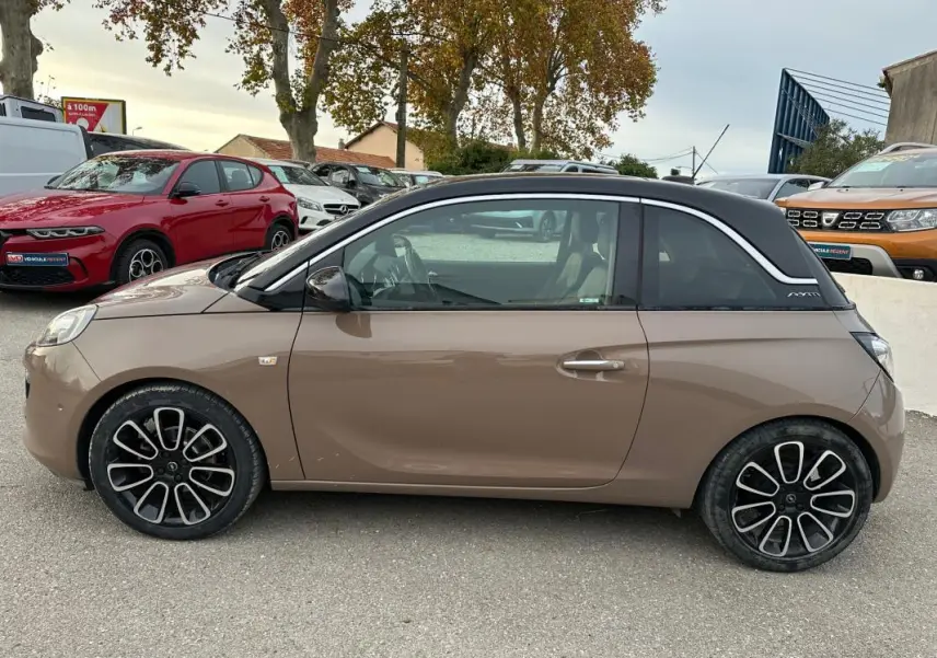 Profil côté gauche d'une Opel Adam marron avec toit noir et jantes alliage 16 pouces, stationnée en extérieur.