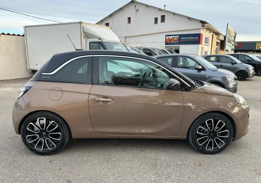 Profil côté gauche d'une Opel Adam marron avec toit noir et jantes alliage 16 pouces sur un parking extérieur.