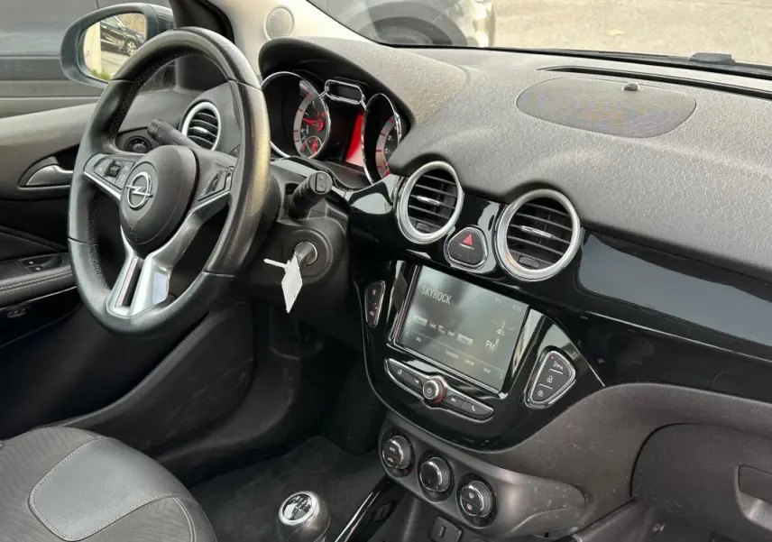 Intérieur de l'Opel Adam 2016 vu côté conducteur, volant cuir multifonctions et écran tactile central noir brillant.
