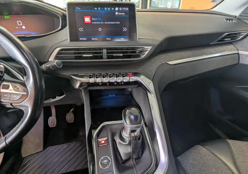 Vue intérieure côté conducteur du tableau de bord et levier de vitesses manuel d’un Peugeot 3008 blanc toit noir, avec écran tactile allumé.