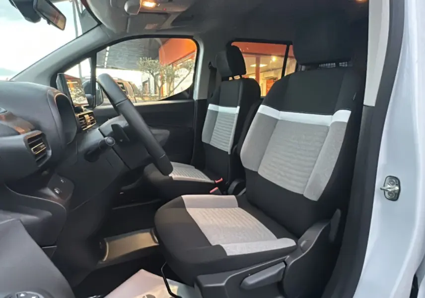 Vue intérieure côté conducteur du Citroën Berlingo 2025, sièges tissu gris et noir avec tableau de bord noir.