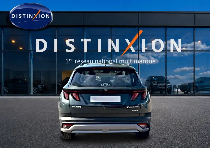 Vue arrière d’un Hyundai Tucson vert hybride 2026, avec feux LED et logo distinctif sur un parking devant un showroom.
