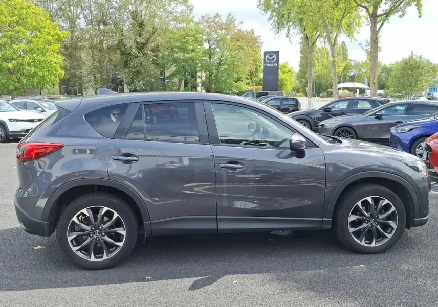Vue latérale côté gauche d'un Mazda CX-5 gris 2015 avec jantes aluminium et vitres surteintées.