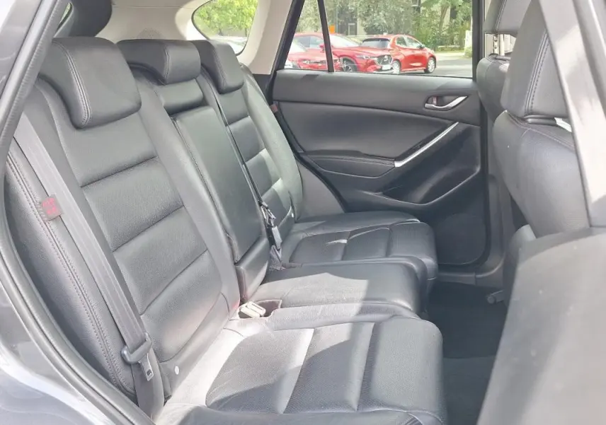 Vue intérieure côté arrière gauche montrant les sièges en cuir noir du Mazda CX-5 gris 2015.
