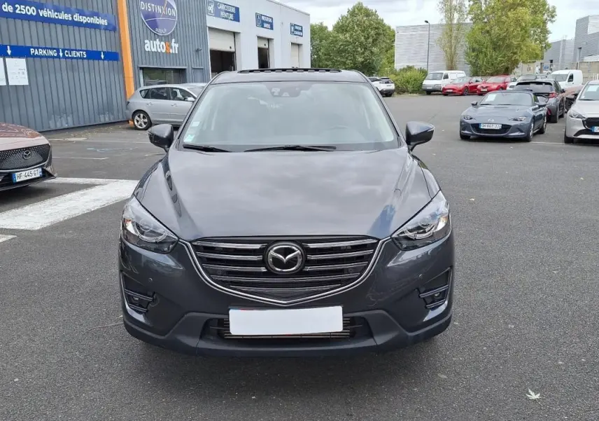 Vue frontale d'un Mazda CX-5 gris 2015 avec calandre chromée et phares LED sur parking extérieur.