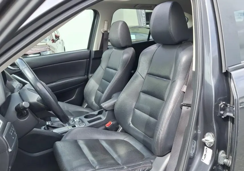 Vue intérieure côté conducteur du Mazda CX-5 gris 2015, sièges en cuir noir et volant multifonctions visible.