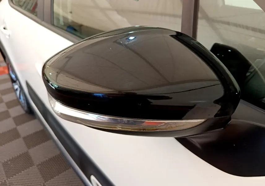 Rétroviseur noir en gros plan côté gauche d'une Citroën C3 blanche, avec clignotant intégré.