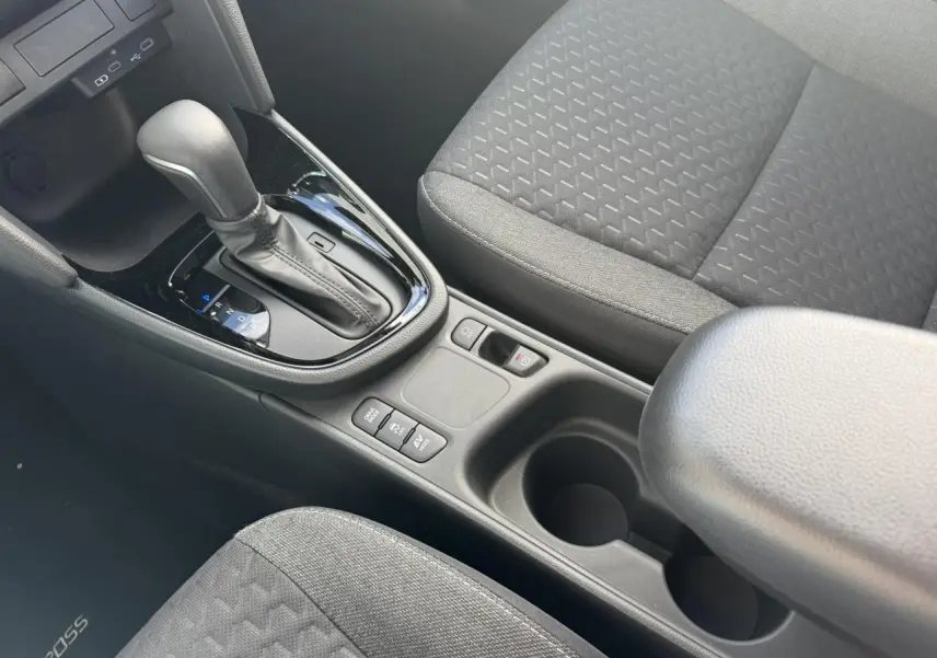 Vue intérieure centrée sur la console centrale et levier de vitesse automatique, sièges tissu gris foncé de la Toyota Yaris Cross.