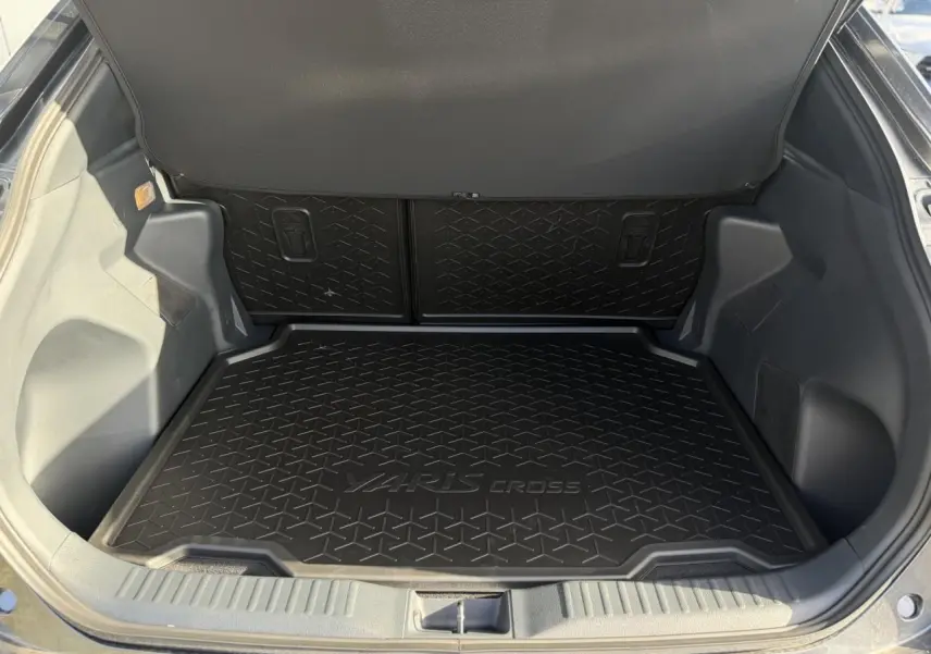 Coffre ouvert de Toyota Yaris Cross gris Atlas, vue plongeante sur tapis de coffre noir avec logo intégré.