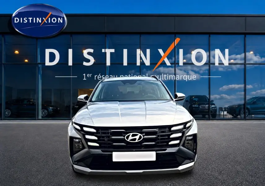 Hyundai Tucson 1.6 t-gdi 239 hybride gris shimmering vu de face devant une vitrine Distinxion.