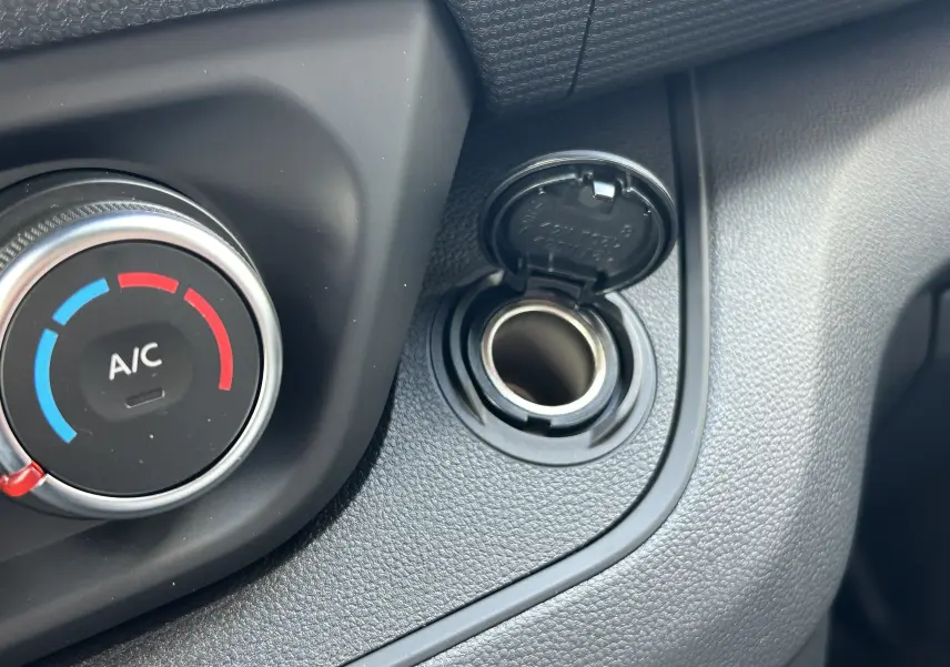 Détail de la prise 12V ouverte et du bouton de réglage de climatisation dans l'habitacle du Renault Trafic Fourgon gris Highland.