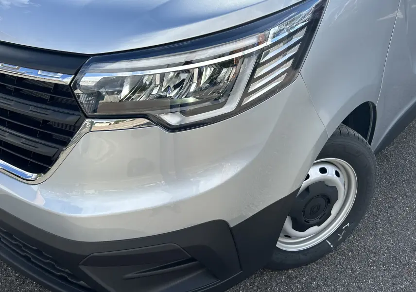 Gros plan sur l'avant droit gris Highland du Renault Trafic Fourgon avec phare moderne et jante acier simple.