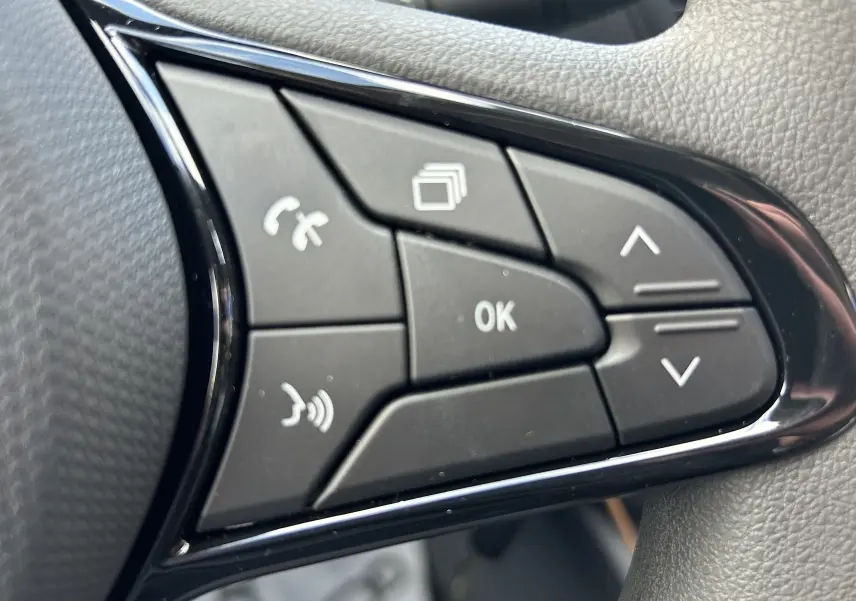 Gros plan sur les commandes multifonctions noires du volant du Renault Trafic Fourgon gris Highland, avec boutons de navigation et appel.