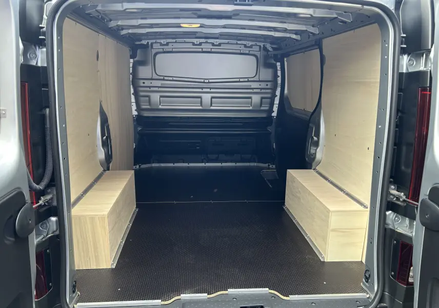 Intérieur arrière du Renault Trafic L1H1 Advance 2025 gris Highland, avec aménagement bois clair et sol noir antidérapant.
