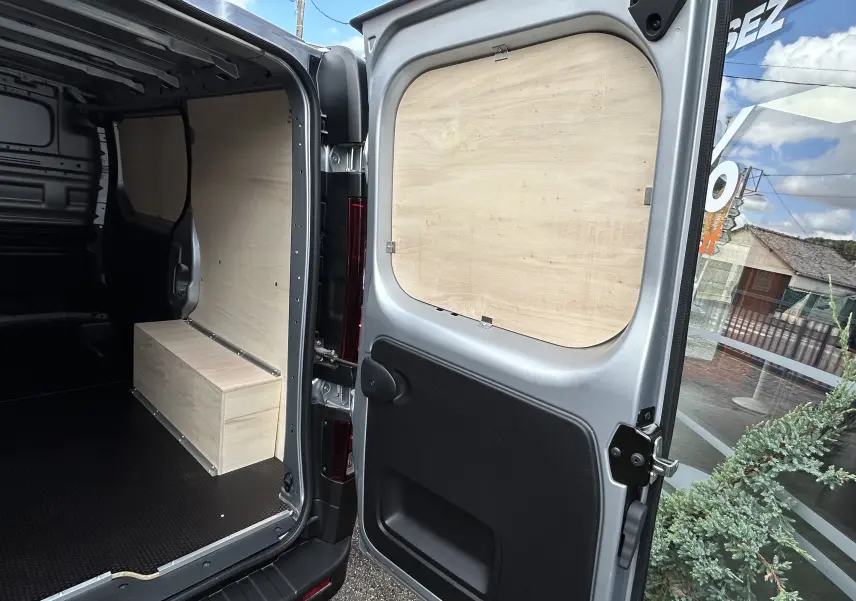 Vue intérieure arrière du Renault Trafic Fourgon gris Highland avec aménagement bois sur porte et parois.