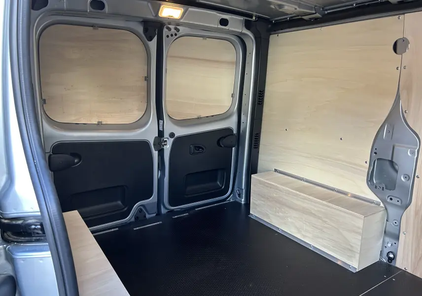 Intérieur arrière du Renault Trafic L1H1 Advance gris Highland, avec aménagement bois et plancher noir antidérapant.