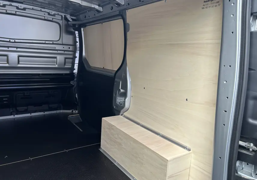 Intérieur du Renault Trafic Fourgon gris Highland vu côté droit, avec aménagement bois clair sur parois et sol noir antidérapant.