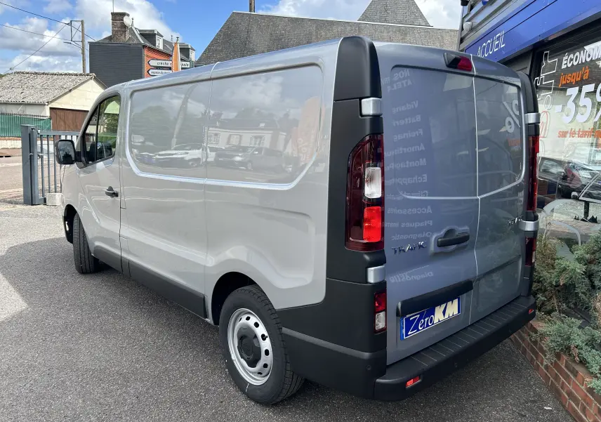 Vue 3/4 arrière droite d’un Renault Trafic Fourgon gris Highland avec portes arrière fermées sur parking urbain.