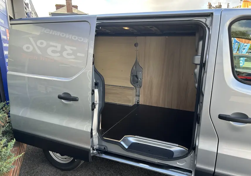 Vue latérale droite d'un Renault Trafic Fourgon gris Highland avec porte coulissante ouverte révélant l'aménagement bois intérieur.