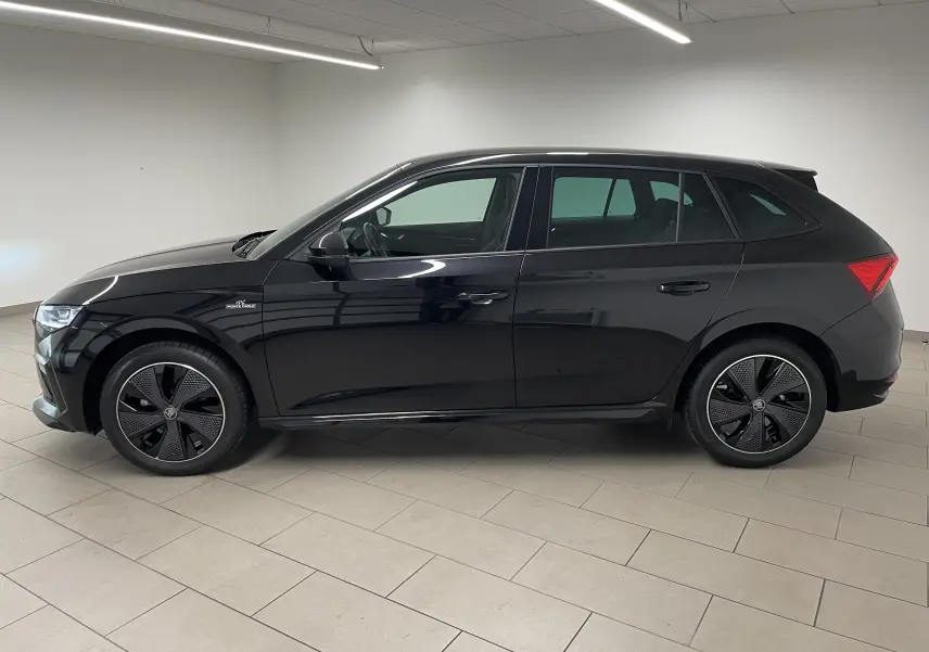 Vue de profil côté gauche d'une Skoda Scala 2025 noire métallisée avec jantes spécifiques Monte-Carlo et double plancher de coffre.