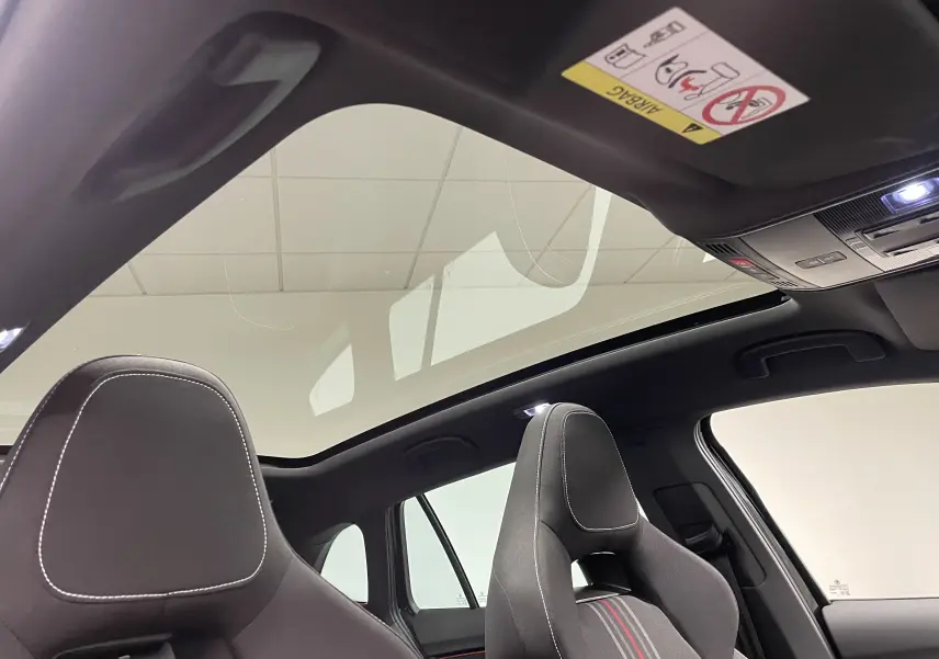 Vue intérieure du toit panoramique et des sièges avant noirs avec surpiqûres blanches de la Skoda Scala 2025.