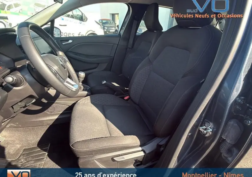 Intérieur avant droit de la Renault Clio gris 2022 montrant sièges tissu noirs et volant avec levier de vitesses manuel.