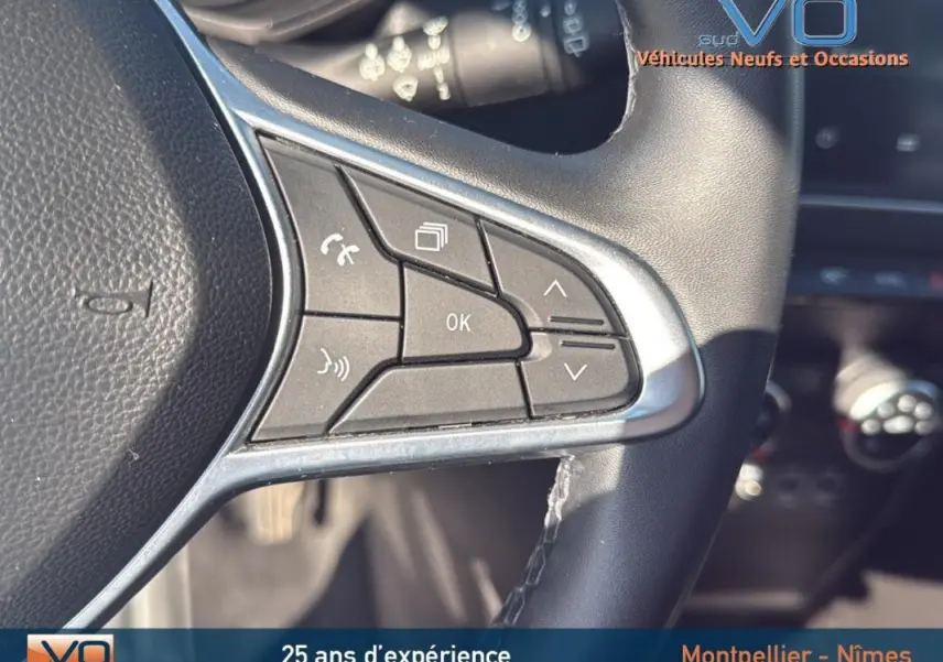 Gros plan sur les commandes multifonctions du volant noir du Renault Clio gris 2022, avec boutons de réglage et appel.