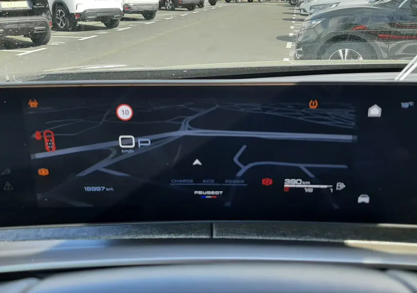 Vue depuis l'intérieur du Peugeot 5008 Hybrid 2025, affichage numérique du tableau de bord avec navigation et compteur.
