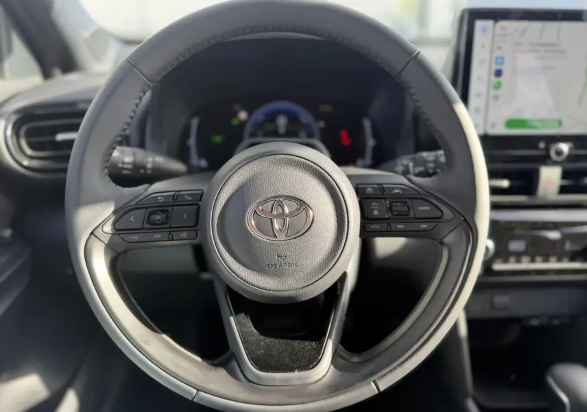 Vue rapprochée du volant multifonctions en cuir de la Toyota Yaris Cross 1.5 Hybrid 130 BVA Design, avec tableau de bord et écran tactile.