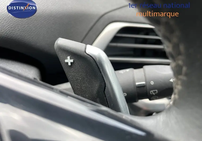 Gros plan sur la palette de changement de vitesse "+" derrière le volant d'un Peugeot 3008 gris, intérieur noir.