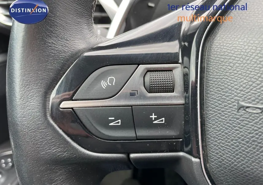 Gros plan sur les commandes du volant en cuir noir du Peugeot 3008 gris, avec boutons de volume et appel mains libres.