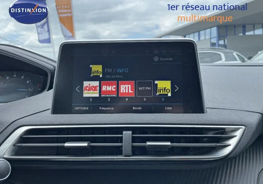 Écran tactile central du tableau de bord du Peugeot 3008 gris Artense, affichant les stations radio FM en extérieur showroom.