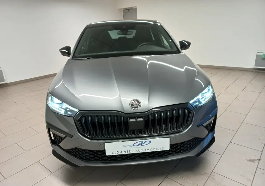 Vue frontale d'une Skoda Scala 1.5 TSI Monte-Carlo gris graphite avec phares allumés en intérieur showroom.