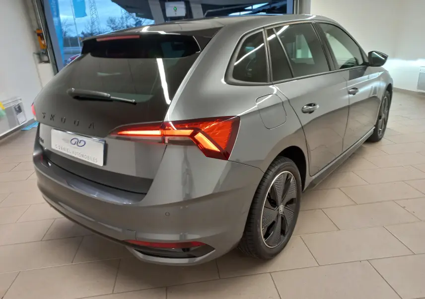 Vue 3/4 arrière droite d'une Skoda Scala 1.5 TSI Monte-Carlo gris graphite avec feux arrière allumés en intérieur showroom.