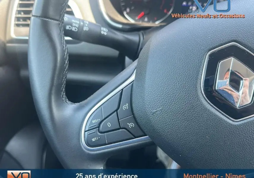 Gros plan sur le volant en cuir de la Renault Mégane IV gris, avec commandes de régulateur de vitesse visibles.