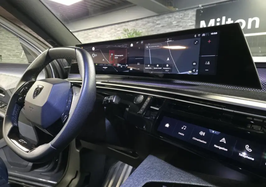 Vue intérieure côté conducteur du tableau de bord noir et écran panoramique du Peugeot 5008 gris hybride 2025.