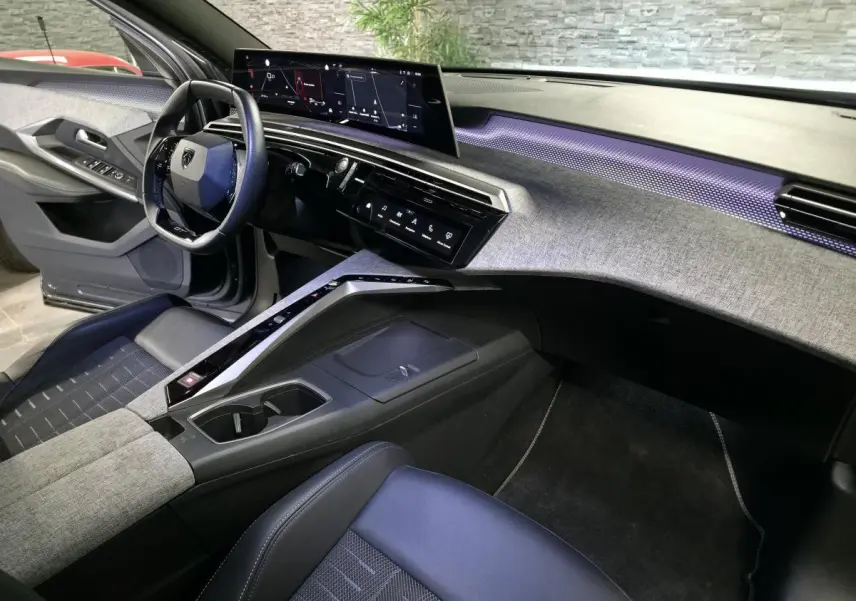 Vue intérieure côté conducteur du Peugeot 5008 gris 2025, avec tableau de bord tissu Rimini chiné et écran panoramique incurvé.